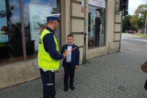 Zdjęcie kolorowe przedstawia policjanta ruchu drogowego rozmawiającego z chłopcem przy przejściu dla pieszych . Zdjęcie z akcji Bezpieczna droga do szkoły
