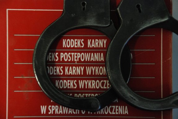 Kolorowa fotografia. Kajdanki policyjne leżące na zbiorze kodeksów, oprawionych w czerwoną obwolutę.