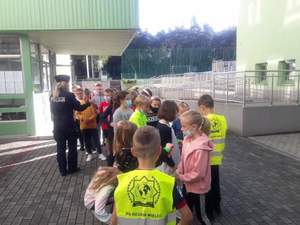 policjantka wraz z dziećmi przed budynkiem szkoły