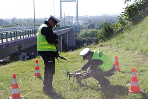 Zdjęcie kolorowe przedstawia dwóch policjantów umundurowanych ruchu drogowego , którzy przygotowują do startu  policyjnego drona