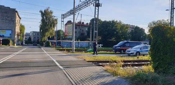 Zdjęcie kolorowe (pora dzienna) , przedstawia przejazd kolejowe z zaporami na ul. Mariackiej w Przemyślu. Po prawej stronie na zdjęciu widoczne są dwa pojazdy 1 pojazd oznakowany Policyjny drugi to oznakowany pojazd SOK. Pojazdy są zaparkowane pomiędzy torowiskiem na drodze technicznej wyłączonej z ruchu.