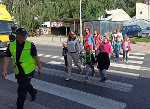 Zdjęcie kolorowe wykonane w porze dziennej przedstawia ul. Czarneckiego w Przemyślu . Na zdjęciu widoczne są dzieci które przechodzą przez przejście dla pieszych , prowadzone przez policjantkę . Po lewej stronie zdjęcia widoczny umundurowany policjant wydziału ruchu drogowego który kieruje ruchem.