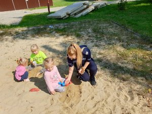 na zdjęciu policjantka bawiąca się w piasku z dwoma kilkuletnimi dziewczynkami