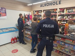 Dwaj policjanci i członek komisji do spraw rozwiązywania problemów alkoholowych kontrolują sklep pod kątem sprzedaży napojów alkoholowych