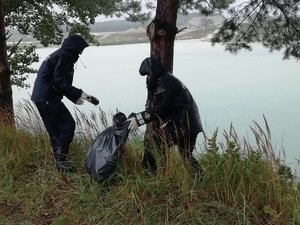 Policjanci nad wodą zbierający zalegające na brzegu śmieci