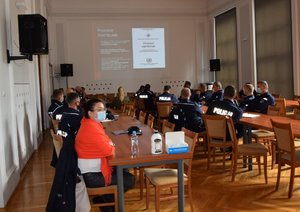 Aula Komendy Wojewódzkiej Policji w Rzeszowie, oraz funkcjonariusze i pracownicy Policji biorący udział w spotkaniu. Na końcu sali, w środkowej części wyświetlona prezentacja