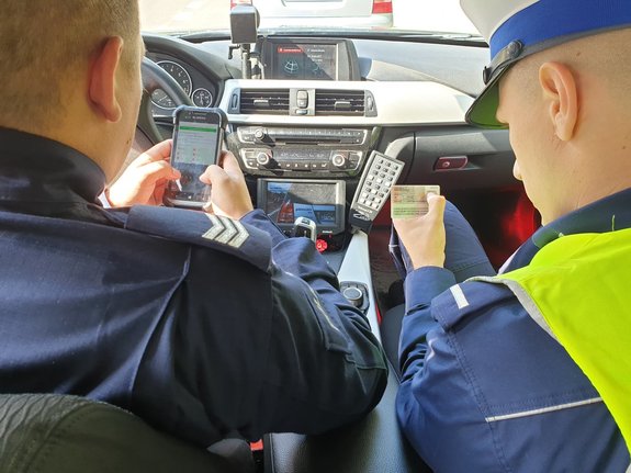 policjanci w czasie kontroli drogowej sprawdzający dokumenty kierującemu, zdjęcie wykonane z wewnątrz radiowozu