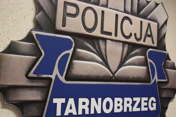 Na zdjęciu widoczne logo Komendy Miejskiej Policji w Tarnobrzegu. Gwiazda policyjna, na tle niebieskiej wstęgi napis w białym kolorze Tarnobrzeg.