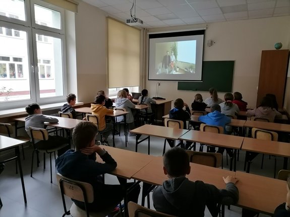 Dzieci siedzące w klasie oglądają film o cyberprzemocy.