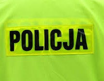 Zdjęcie kolorowe przedstawia tył kamizelki odblaskowej w kolorze rażąco żółtym na którym widnieje napis &quot;POLICJA&quot; w czarnym kolorze