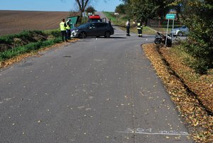 Zdj ecie kolorowe wykonane w porze dziennej-przedstawia skrzyżowanie w gminie Fredropol miejsce zdarzenia drogowego. W oddali zdjęcia po lewej stronie widoczny jest samochód osobowy peugeot w kolorze srebrnym przy którym stoi dwóch policjantów umundurowanych . Po prawej stronie widoczny motocykl który zaparkowany jest na znaku drogowym z napisem DAROWICE. Po środku widoczny jest strażak oraz nn mężczyzna