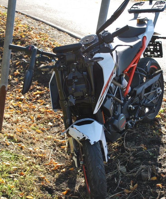 Zdjęcie kolorowe przedstawia motocykl KTM 125 Duke z uszkodzeniami pokolizyjnymi . Motocykl jest w kolorach biało -czerwonych