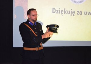 Funkcjonariusz prezentuje umundurowanie, w ręku trzyma policyjną czapkę