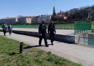 Zdjęcie kolorowe wykonane w porze dziennej-przedstawia dwóch funkcjonariuszy policji umundurowanych w trakcie patrolu deptaka przy ul. Wybrzeże Jana Pawła II w Przemyślu.