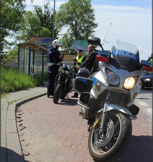 policyjny motocykl, za nim dwoje policjantów prowadzących kontrolę