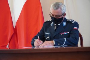 Komendant Wojewódzki Policji w Rzeszowie insp. Dariusz Matusiak podpisuje dokument porozumienia. W tle biało-czerwone flagi