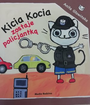 Zdjęcie przedstawia ilustracje książeczki dla dzieci pt:&quot;Kicia Kocia zostaje policjantką. Okładka jest w żółtym kolorze z obrazową ob ramówką . Po prawej stronie jest rysunek kotki która w prawej ręce trzyma kajdanki i jest umundurowana , po lewej stronie rysunki dwóch aut. W lewym górnym rogu umieszczony jest tytuł książeczki &quot;Kicia Kocia( w czarnym kolorze) zostaje policjantką w kolorze czerwonym. Na dole rysunku widoczny radiotelefon .