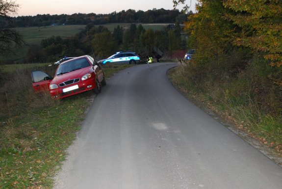 Zdjęcie kolorowe wykonane w porze nocnej-przedstawia miejsce zdarzenia drogowego w miejscowości Zalesie. Na pierwszym planie widoczny samochód m-ki daewoo lanos w kolorze czerwonym który jest zaparkowany na łuku drogi . Za im widoczny radiowóz oznakowany policyjny oraz widoczny jest policjant  ubrany w kamizelkę odblaskową .