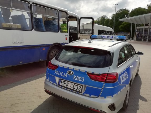Policjant Wydziału Ruchu Drogowego stoi na schodach autobusu miejskiego. Obok autobusu stoi oznakowany radiowóz.