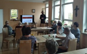 Zdjęcie przedstawia pomieszczenie, w którym znajdują się osoby i funkcjonariusz, który uczestniczy w spotkaniu