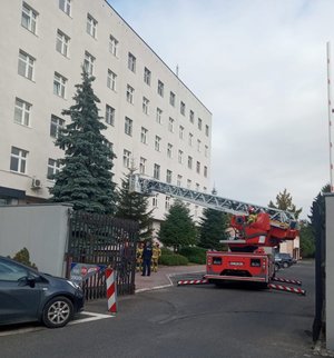 Zdjęcie korowe wykonane w porze dziennej-przedstawia budynek Komendy Miejskiej Policji w Przemyślu , przed budynkiem zaparkowany jest wóz strażacki, z którego wypuszczana jest drabina . Trwają ćwiczenia przeciwpożarowe.