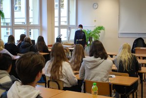 Na zdjęciu w klasie stojąca przodem do uczniów kom. Renata Bednarska prowadzi prelekcję. Na pierwszym planie siedzacy w ławkach uczniowie.