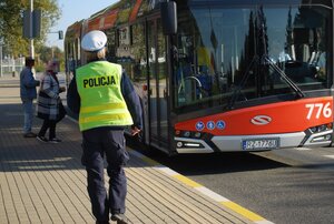 Policjantka podchodzi do autobusu komunikacji miejskiej. Do autobusu wsiadają dwie osoby