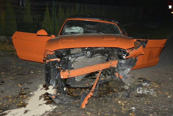 Zdjęcie wykonane w porze nocnej -  przedstawia miejsce zdarzenia drogowego w miejscowości Buszkowiczki . Na zdjęciu widoczny jest pojazd marki ford mustang koloru pomarańczowego z rozbitym przodem pojazdu