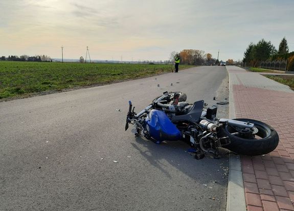 Motocykl biorący udział w zdarzeniu lezy na drodze. W tle policjant