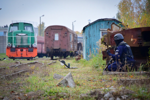 Policjanci oddziału prewencji w kasku schowany za żelaznymi elementami (po prawej stronie). W tle na środku lokomotywa i wagon kolejowy.