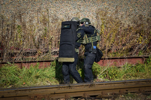 Uzbrojeni policyjni kontrterroryści schowani za tarczą idą wzdłuż torów kolejowych