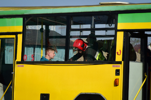 Widok przez okno autobusu. Wewnątrz strażacy udzielający pomocy poszkodowanym