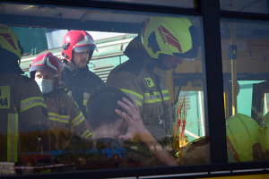 Widok przez okno autobusu. Wewnątrz strażacy udzielający pomocy poszkodowanym