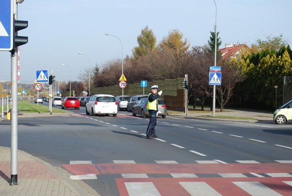 Na zdjęciu umundurowany policjant ruchu drogowego na skrzyżowaniu reguluje ruchem.