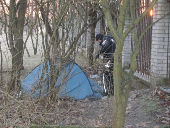 Policjant stoi obok namiotu rozłożonego między drzewami