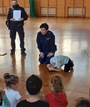 Policjantka demonstruje na przykładzie ucznia jaką przyjąć bezpieczną  postawę  w przypadku ataku niebezpiecznego zwierzęcia