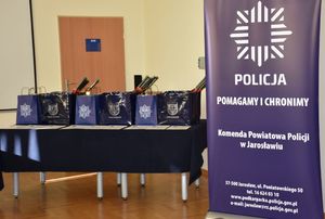 Baner Komendy Powiatowej Policji w Jarosławiu obok którego na stole znajdują się nagrody dla laureatów konkursu plastycznego.