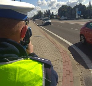 Policjant sprawdzający prędkość kierowców jadących drogą krajową nr 94 . w tle samochody i rowerzysta jadący chodnikiem