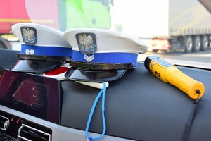 Dwie policyjne czapki funkcjonariuszy ruchu drogowego oraz urządzenie alcoblow służące do sprawdzania stanu trzeźwości, położone na desce rozdzielczej radiowozu
