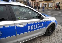 Zdjęcie kolorowe wykonane w porze dziennej przedstawia lewą stronę pojazdu oznakowanego policyjnego zaparkowanego przy ul. Grunwaldzkiej w Przemyślu.
