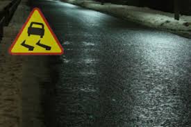 Zdjęcie wykonane w porze nocnej-przedstawia nawierzchnie drogi-  z lewej strony fotografii jest umieszczony znak drogowy ostrzegawczy w kształcie żółtego trójkąta „uwaga śliska nawierzchnia” . Na znaku jest umieszczony samochód w kolorze czarnym a pod spodem dwie czarne załamane linie .