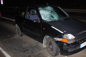 Zdjęcie kolorowe wykonane w porze nocnej, przedstawia miejsce zdarzenia drogowego (potrącenie pieszego) w miejscowości Bircza. Na zdjęciu jest widoczny pojazd m-ki Fiat koloru granatowego , który ma rozbita szybę czołową.