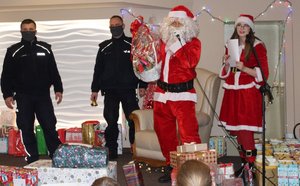 Na zdjęciu widoczny Mikołaj, pomocnica Mikołaja i dwaj umundurowani policjanci stojący na scenie wśród prezentów.