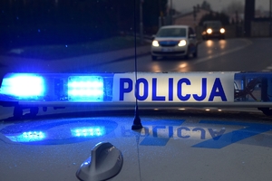 Policyjna belka na radiowozie z włączonym oświetleniem. W tle światła przejeżdżających pojazdów.