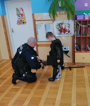Policjant zakłada dziecku kamizelkę taktyczną i hełm.