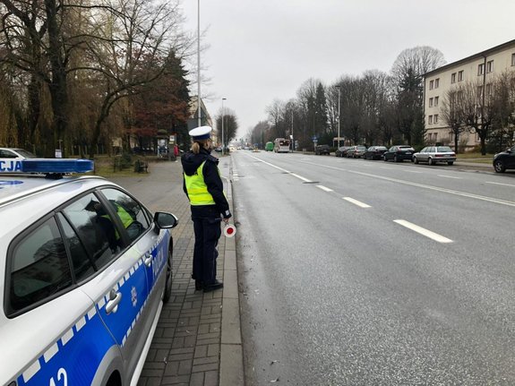 Na zdjęciu umundurowana policjantka ruchu drogowego na punkccie kontrolnym przy ul. Cieplińskiego. Na pierwszym planie widac zaparkowany radiowóz. W tle ulica Cieplińskiego.