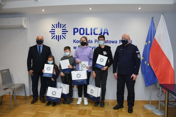 Zdjęcie grupowe - od lewej stoi Starosta Powiatu Ropczycko - Sędziszowskiego, następnie czworo laureatów konkursu. po prawej stronie stoi Komendat Powiatowy Policji w Ropczycach,