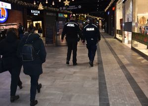 Policjant i strażnik miejski przechodzą przez pasaż galerii handlowej
