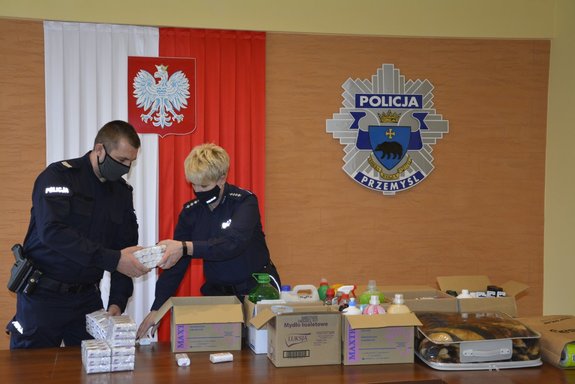 Zdjęcie wykonane w  porze dziennej , przedstawia świetlicę komendy Miejskiej Policji w Przemyślu. Na zdjęciu widoczni są policjanci , którzy na stołach układają prezenty dla seniorów z hospicjum &quot;Santa Rita&quot; w Przemyślu