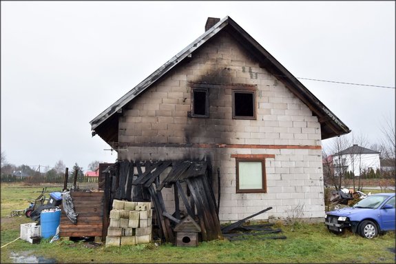 Pożar domu jednorodzinnego gmina Baranów Sandomierski. Dom z białego pustaka, na ścianach czarne ślady dymu, przy domu resztki spalonej drewnianej szopy.